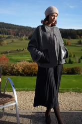 a lady in a grey wool coat and a black pleated skirt